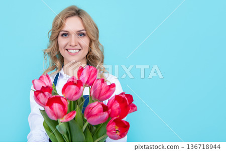 smiling girl in apron with spring tulip flowers on blue background 136718944