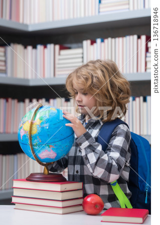 Pupil looking at globe in library at the elementary school. Back to school. Portrait of cute child school boy. Clever kid with school supplies. Pupil looking at globe in library at the elementary school. Back to school. Portrait of cute child school boy. Clever kid with school supplies. 136718946