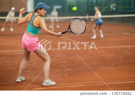 Young female tennis player engrossed in doubles on clay court 136719082