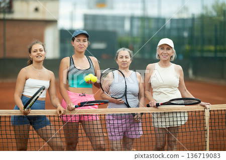 Group of cheerful female tennis players posing on clay court 136719083