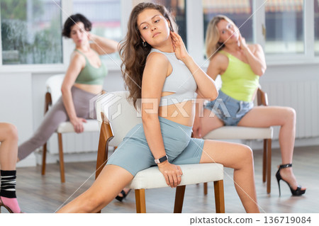 Group of women in high heels rehearsing dance while sitting on chair 136719084