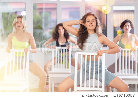 Group of girls unleash their energy and dance passionately near a chair in high heels in a dance studio. His powerful moves combined with elegance of high heels 136719098