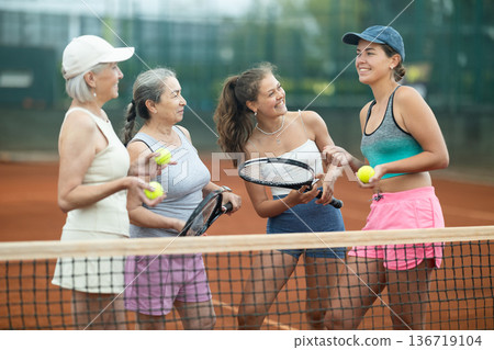 Cheerful female tennis players chatting after match on court 136719104
