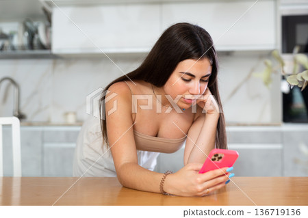 Young woman reading message on phone in kitchen 136719136