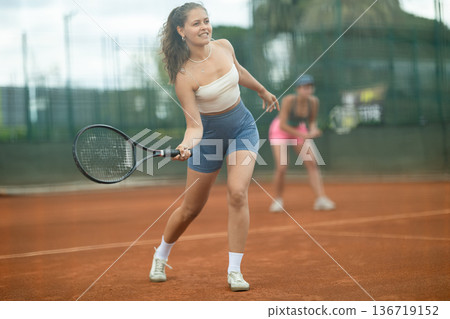 Sporty young girl playing doubles tennis on outdoor court 136719152
