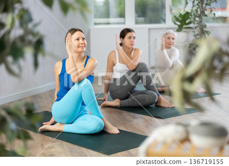 Active fit women twisting on mats while performing stretching exersice Marichyasana or Marichi Position during yoga class together Active fit women twisting on mats while performing stretching exersice Marichyasana or Marichi Position during yoga class together 136719155