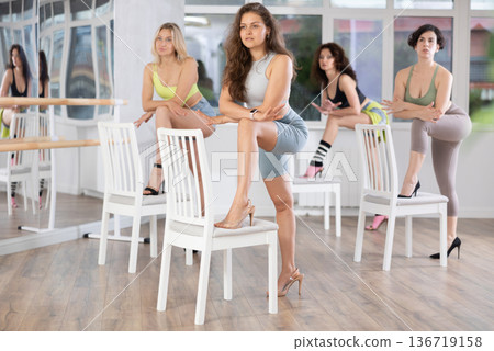 Group of women in high heels rehearsing dance with their feet on chair Group of women in high heels rehearsing dance with their feet on chair 136719158