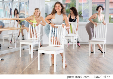 Young woman stands next to chair, leans on back and performs set of lap dance movements Young woman stands next to chair, leans on back and performs set of lap dance movements 136719166