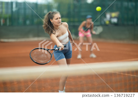 Fit girl engrossed in doubles tennis game on clay court Fit girl engrossed in doubles tennis game on clay court 136719227