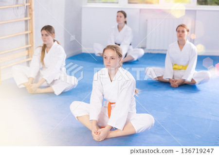 Butterfly pose - teenage girls in white kimono practices stretching in gym 136719247
