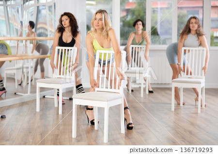Young woman stands next to chair, leans on back and performs set of lap dance movements Young woman stands next to chair, leans on back and performs set of lap dance movements 136719293