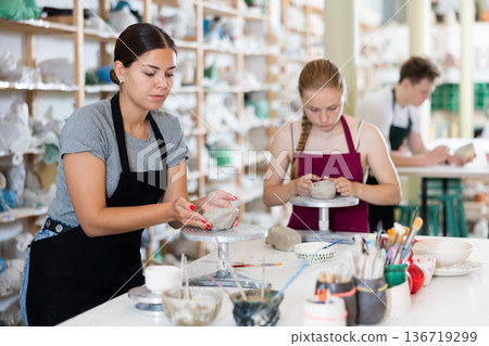 Pottery teacher together with young students sculpt dishes from clay Pottery teacher together with young students sculpt dishes from clay 136719299