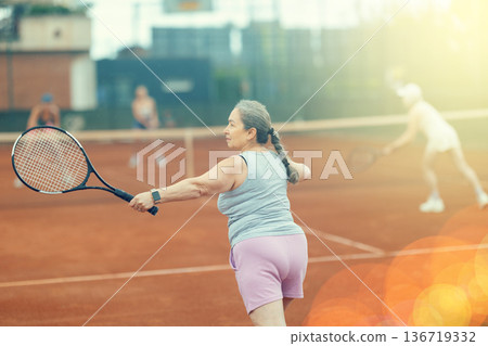 Two elderly women playing tennis against young women 136719332