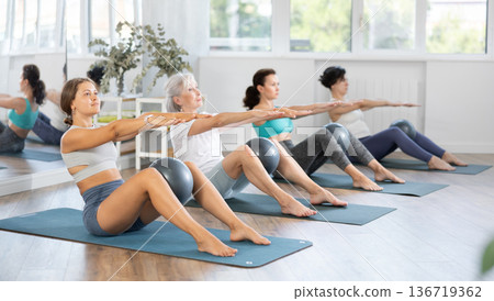 Woman performing set of exercises with pilates balls during group class with of different ages in fitness studio Woman performing set of exercises with pilates balls during group class with of different ages in fitness studio 136719362