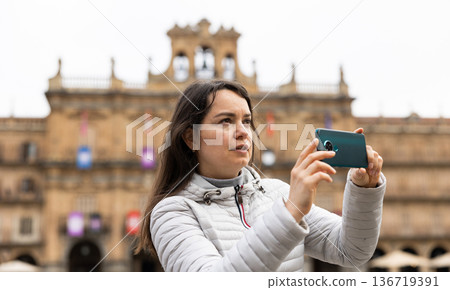 Woman is taking photos on her camera while journey through the Plaza Mayor. Spain Woman is taking photos on her camera while journey through the Plaza Mayor. Spain 136719391