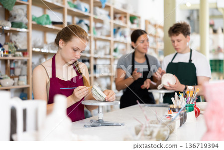 Young woman teaches teenage boy and teenage girl to paint ceramic cup Young woman teaches teenage boy and teenage girl to paint ceramic cup 136719394