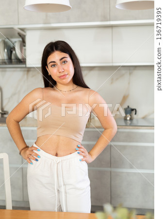 Smiling young woman posing against background of white kitchen Smiling young woman posing against background of white kitchen 136719395