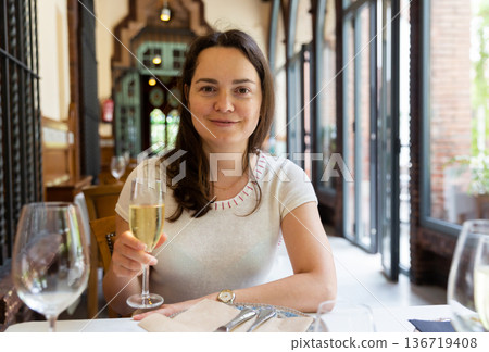 Dreamy woman with glass of wine at table in restaurant Dreamy woman with glass of wine at table in restaurant 136719408