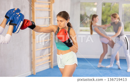Girls works out strength and speed of boxing punch mitts with help of partner in boxing paws Girls works out strength and speed of boxing punch mitts with help of partner in boxing paws 136719413