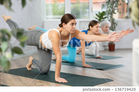 Woman doing yoga with group in fitness studio, standing in stretching asana Mukha Shvanasana 136719420