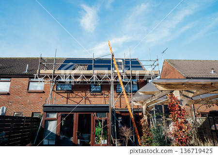 Construction project to install solar panels on a house using scaffolding with blue sky background. Modern, energy-efficient house. Renewable eco Energy. Smart energy management. Construction project to install solar panels on a house using scaffolding with blue sky background. Modern, energy-efficient house. Renewable eco Energy. Smart energy management. 136719425