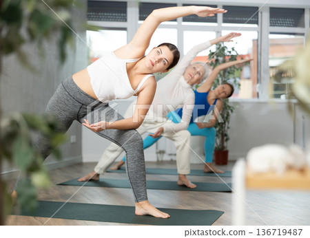 Sporty woman doing standing forward bend Uttanasana, effective yoga pose for back flexibility in group workout Sporty woman doing standing forward bend Uttanasana, effective yoga pose for back flexibility in group workout 136719487