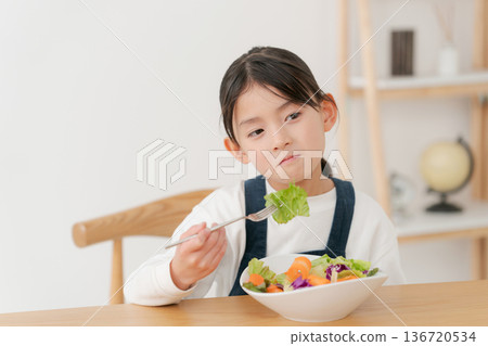 A girl eating vegetables she doesn't like A girl eating vegetables she doesn't like 136720534