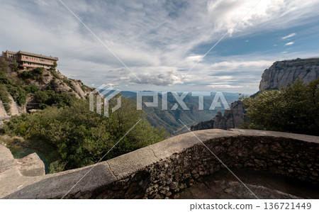 panoramic view from a stone lookout point at Montserrat, Spain. Featuring rugged mountains, a building on a cliff, and a vast valley under a cloudy blue sky. panoramic view from a stone lookout point at Montserrat, Spain. Featuring rugged mountains, a building on a cliff, and a vast valley under a cloudy blue sky. 136721449
