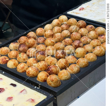 Takoyaki, a popular Japanese street food, are crispy round dough balls filled with octopus, tempura bits, and pickled ginger, topped with takoyaki sauce, bonito flakes, and aonori. Takoyaki, a popular Japanese street food, are crispy round dough balls filled with octopus, tempura bits, and pickled ginger, topped with takoyaki sauce, bonito flakes, and aonori. 136722808