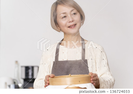 A senior woman steaming sweet potato buns in a bamboo steamer in the kitchen A senior woman steaming sweet potato buns in a bamboo steamer in the kitchen 136724033