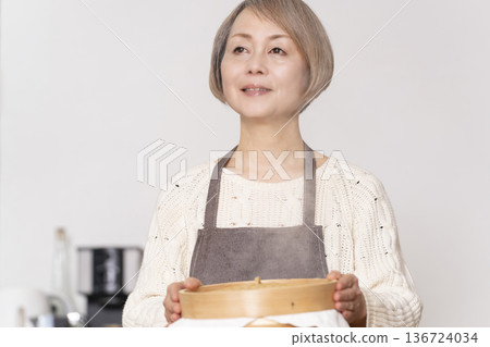 A senior woman steaming sweet potato buns in a bamboo steamer in the kitchen 136724034