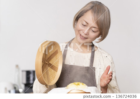 A senior woman steaming sweet potato buns in a bamboo steamer in the kitchen A senior woman steaming sweet potato buns in a bamboo steamer in the kitchen 136724036