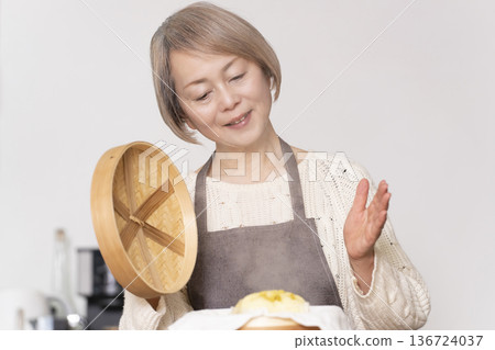 A senior woman steaming sweet potato buns in a bamboo steamer in the kitchen 136724037
