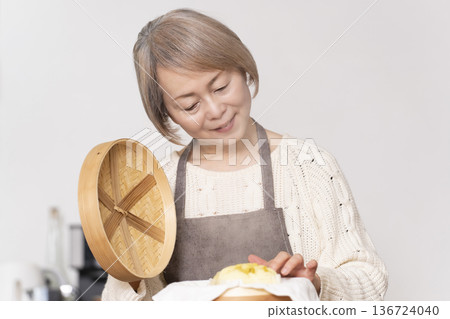 A senior woman steaming sweet potato buns in a bamboo steamer in the kitchen A senior woman steaming sweet potato buns in a bamboo steamer in the kitchen 136724040