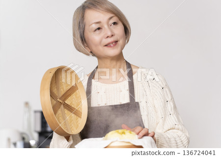 A senior woman steaming sweet potato buns in a bamboo steamer in the kitchen A senior woman steaming sweet potato buns in a bamboo steamer in the kitchen 136724041