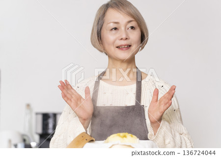 A senior woman steaming sweet potato buns in a bamboo steamer in the kitchen 136724044