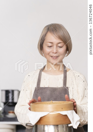 A senior woman steaming sweet potato buns in a bamboo steamer in the kitchen 136724046