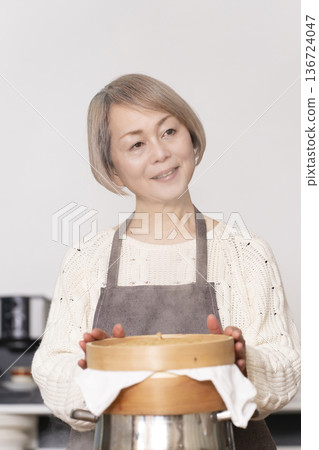 A senior woman steaming sweet potato buns in a bamboo steamer in the kitchen A senior woman steaming sweet potato buns in a bamboo steamer in the kitchen 136724047