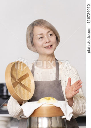A senior woman steaming sweet potato buns in a bamboo steamer in the kitchen A senior woman steaming sweet potato buns in a bamboo steamer in the kitchen 136724050