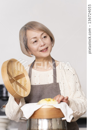 一位老婦人在廚房裡用竹蒸籠蒸地瓜包。 一位老婦人在廚房裡用竹蒸籠蒸地瓜包。 136724055