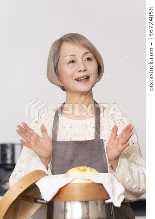 A senior woman steaming sweet potato buns in a bamboo steamer in the kitchen 136724058