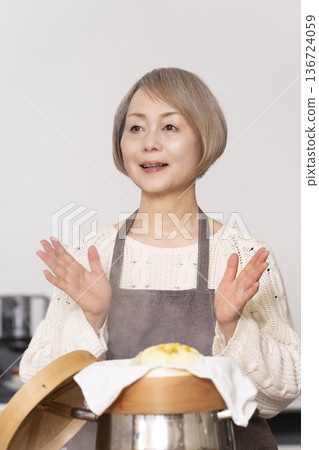 一位老婦人在廚房裡用竹蒸籠蒸地瓜包。 136724059