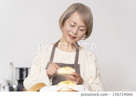 一位老婦人在廚房裡用竹蒸籠蒸地瓜包。 136724060
