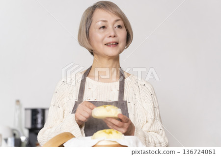 一位老婦人在廚房裡用竹蒸籠蒸地瓜包。 136724061