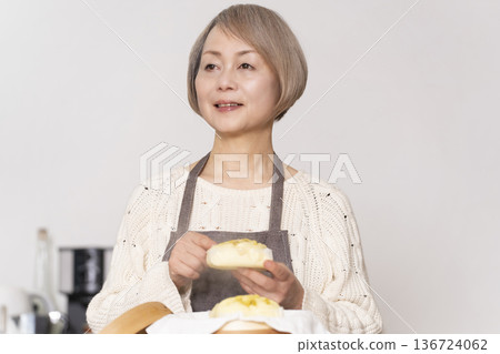 A senior woman steaming sweet potato buns in a bamboo steamer in the kitchen A senior woman steaming sweet potato buns in a bamboo steamer in the kitchen 136724062