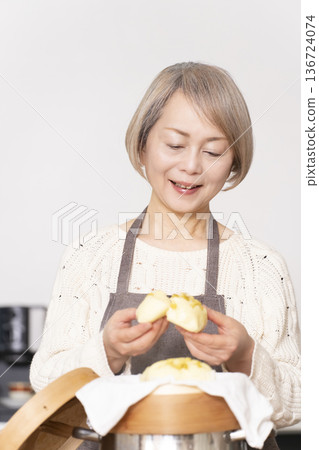 A senior woman steaming sweet potato buns in a bamboo steamer in the kitchen A senior woman steaming sweet potato buns in a bamboo steamer in the kitchen 136724074
