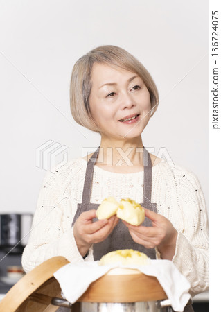 A senior woman steaming sweet potato buns in a bamboo steamer in the kitchen A senior woman steaming sweet potato buns in a bamboo steamer in the kitchen 136724075