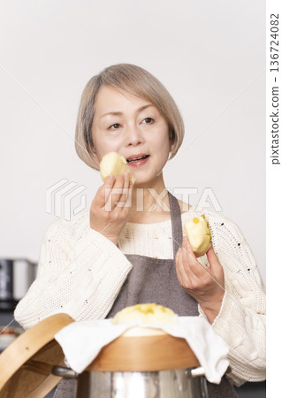 一位老婦人在廚房裡用竹蒸籠蒸地瓜包。 一位老婦人在廚房裡用竹蒸籠蒸地瓜包。 136724082