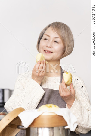 A senior woman steaming sweet potato buns in a bamboo steamer in the kitchen A senior woman steaming sweet potato buns in a bamboo steamer in the kitchen 136724083