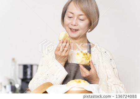 一位老婦人在廚房裡用竹蒸籠蒸地瓜包。 136724088